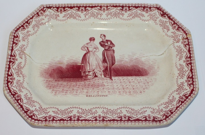 Längliche Platte mit rotem Dekor; Herzog Wellington tanzt mit der Herzogin von Richmond. Ein großer Sprung in Längsrichtung.